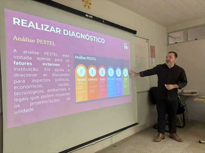 Alexandre Nogueira, diretor da Divisão de Gestão Estratégica, ao lado de uma imagem projetada em tela branca